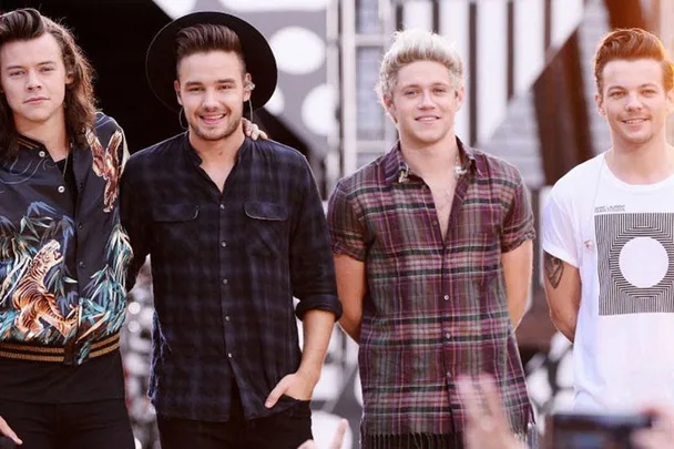 Members of the band One Direction standing together and smiling during an outdoor event.