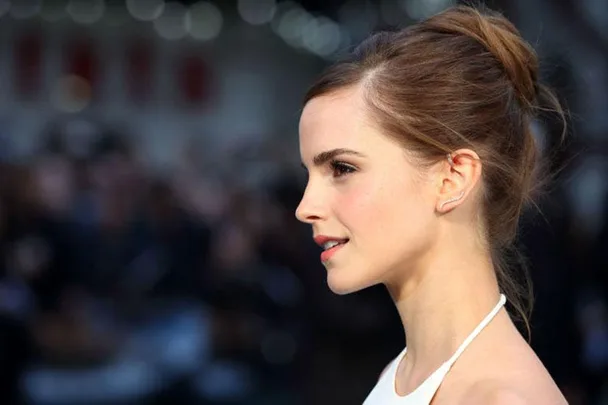 Actress Emma Watson at a public event, wearing an elegant updo and white halter dress.