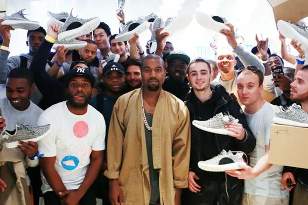 Kanye West stands with fans holding Yeezy Boost 350 sneakers, celebrating his Shoe of the Year award.