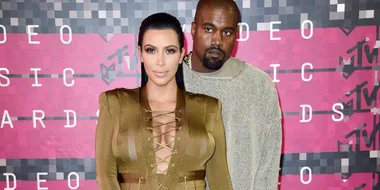 A woman in a brown lace-up dress and a man in a grey sweater on a red carpet at the MTV Video Music Awards.