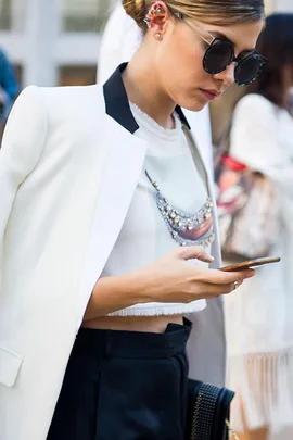 Woman in a stylish white jacket and large sunglasses looks at her phone.