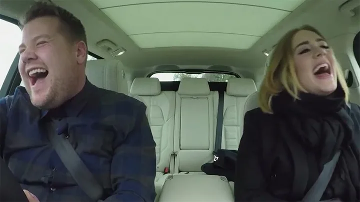 James Corden and Adele laughing together while filming "Carpool Karaoke" segment inside a car.