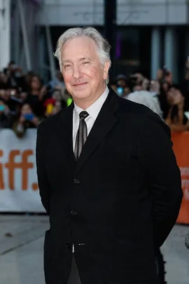 Alan Rickman, known for his role as Severus Snape in the Harry Potter series, at a public event, dressed in a black suit.