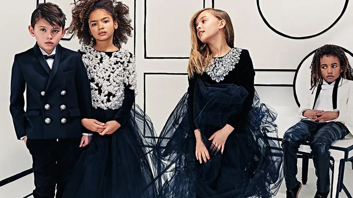 Children modeling Balmain's luxury childrenswear; boys in black double-breasted blazer, and white tuxedo, girls in embellished dresses.