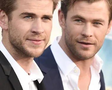 Two men wearing suits stand side by side at a red carpet event, gazing to their left.