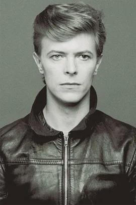 Monochrome photo of David Bowie wearing a leather jacket, looking directly at the camera with a neutral expression.