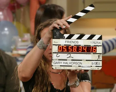 Behind-the-scenes of Friends with a clapperboard; Joey and Rachel are visible in the background.