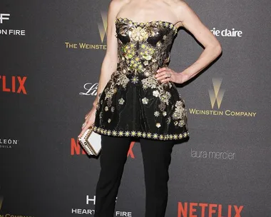 Woman in a black strapless floral peplum top with black pants at a Netflix event, holding a clutch.