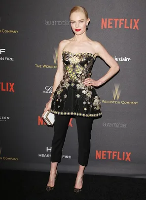 Woman in a black strapless floral peplum top with black pants at a Netflix event, holding a clutch.