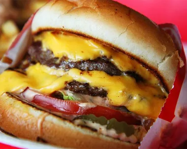 Close-up of an In-N-Out Burger with two beef patties, cheese, lettuce, tomato, pickles, and sauce on a toasted bun.