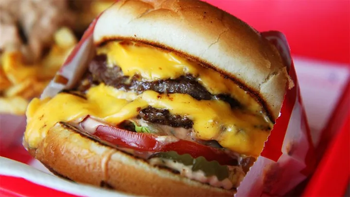 Close-up of an In-N-Out Burger with two beef patties, cheese, lettuce, tomato, pickles, and sauce on a toasted bun.