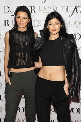 Kendall and Kylie Jenner at a red carpet event, both wearing black crop tops and dark pants.