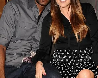 Khloe Kardashian and Lamar Odom sitting together, smiling, with their arms around each other at a public event.