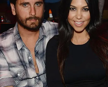 A man in a plaid shirt and a woman in a black top are sitting close together, smiling at the camera.