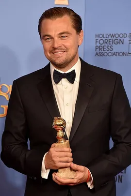 Leonardo DiCaprio in a black suit holding a Golden Globe award, with a smile on his face in front of a blue background.