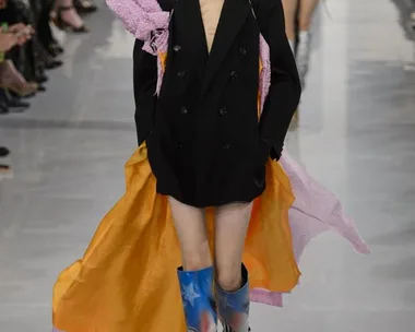 Model in black coat with orange and pink layers, star-patterned boots, at Maison Margiela Haute Couture SS16 show.