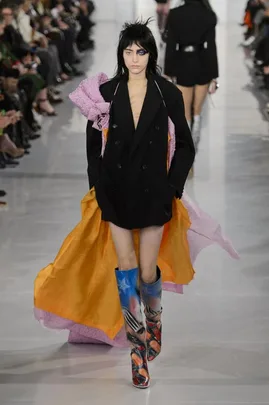 Model in black coat with orange and pink layers, star-patterned boots, at Maison Margiela Haute Couture SS16 show.