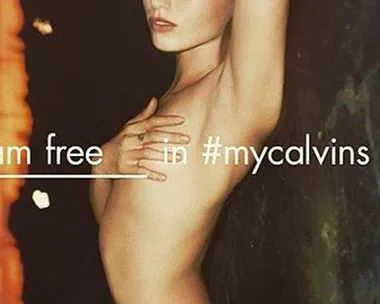 Young woman posing topless in Calvin Klein jeans, with arms up and text "I am free in #mycalvins."