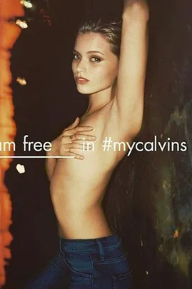 Young woman posing topless in Calvin Klein jeans, with arms up and text "I am free in #mycalvins."
