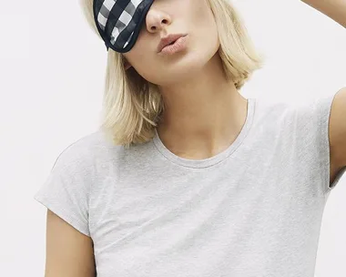 A person wearing a grey t-shirt holds up a black and white checkered sleep mask labeled "Country Road".