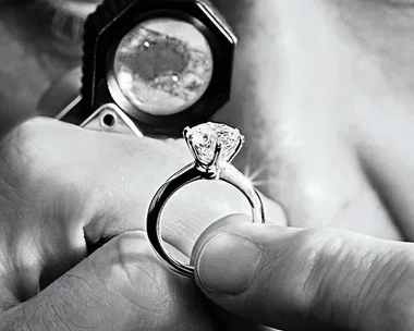 A gemologist examining a diamond ring with a loupe, celebrating 130 years of the Tiffany Setting.