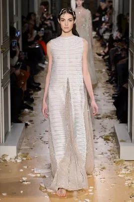 Model in a textured white and silver Valentino gown walks down a petal-strewn runway during the SS16 haute couture show.