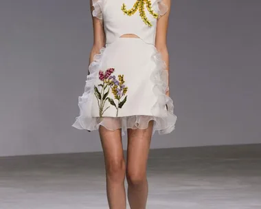 Model wearing Giambattista Valli SS16 couture: white dress with floral embroidery and ruffled details on runway.