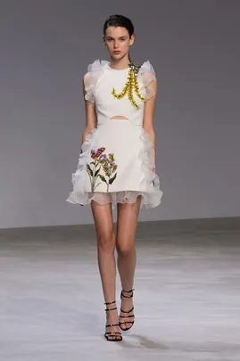 Model wearing Giambattista Valli SS16 couture: white dress with floral embroidery and ruffled details on runway.