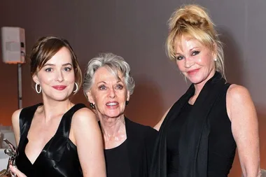 Dakota Johnson, Tippi Hedren, and Melanie Griffith smiling and posing together, all wearing black outfits at an event.