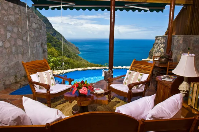Luxury patio with wooden chairs and small pool overlooking the sea and lush mountains.