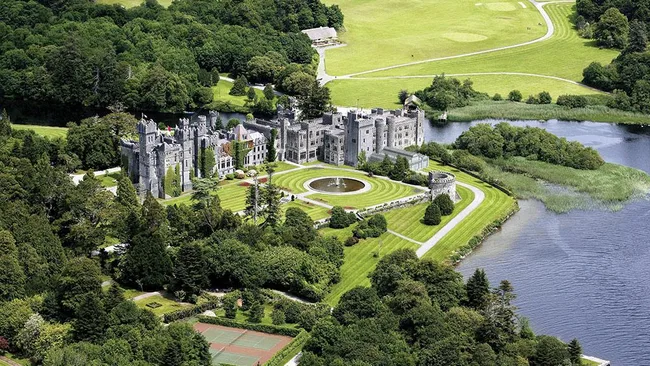 Aerial view of Ashford Castle surrounded by lush greenery and a lake.