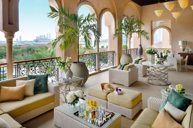 Luxurious veranda with plush seating, potted plants, city view, and elegant decor under ornate arches.