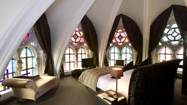 Luxurious bedroom with arched windows, stained glass, a plush bed, and elegant decor.