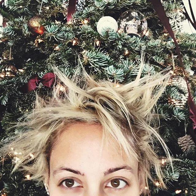 Woman with spiky blond hair in front of a decorated Christmas tree.