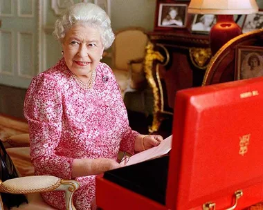 Queen Elizabeth II is seated at her desk in her private audience room at Buckingham Palace with one of her official red boxes.