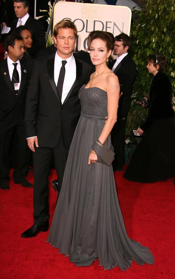 Two people in formal attire pose on a red carpet at an event, surrounded by other attendees.