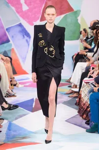 Model in black dress with gold face embroidery, thigh-high slit, Schiaparelli Fall 2016 Haute Couture runway.