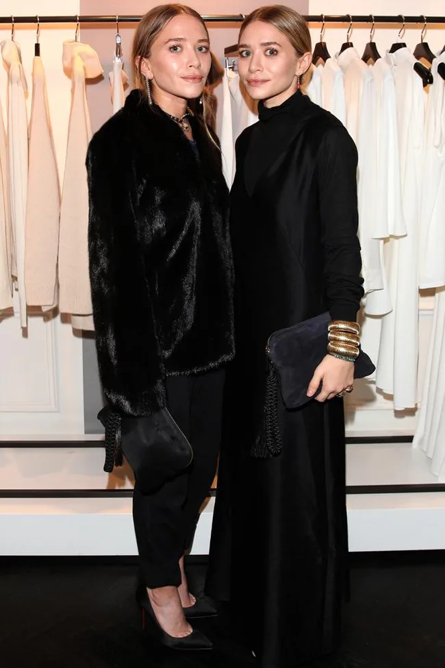 Two women in black outfits standing in a clothing store with white garments in the background.