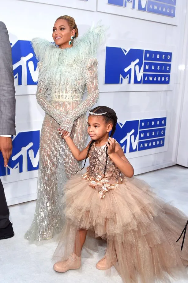 Beyoncé in a feathered gown with a young girl in a tulle dress at the MTV Video Music Awards red carpet event.