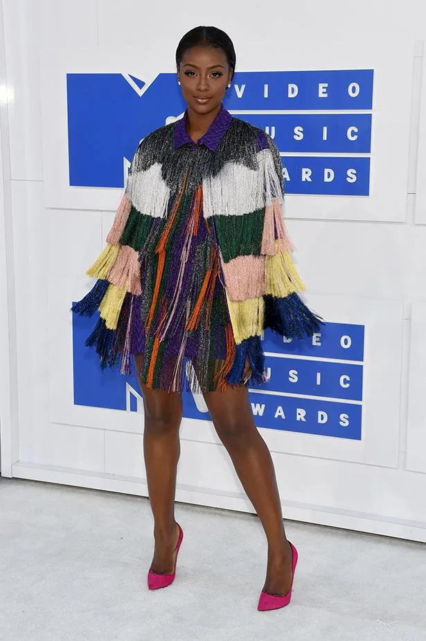 A person in a multicolored fringed outfit and pink heels poses at the Video Music Awards.