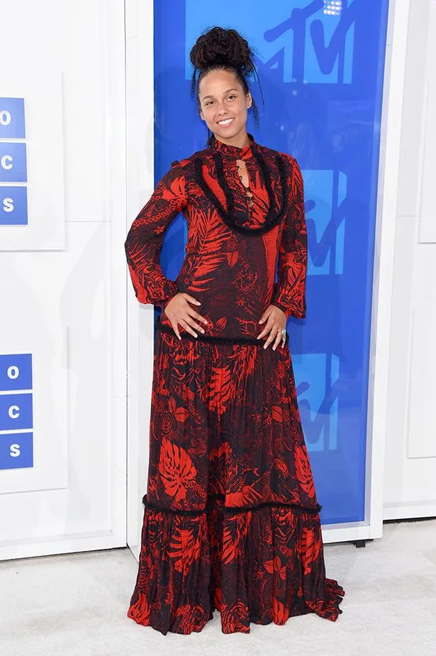 A person wearing a long red and black floral dress poses in front of an MTV backdrop at an event.