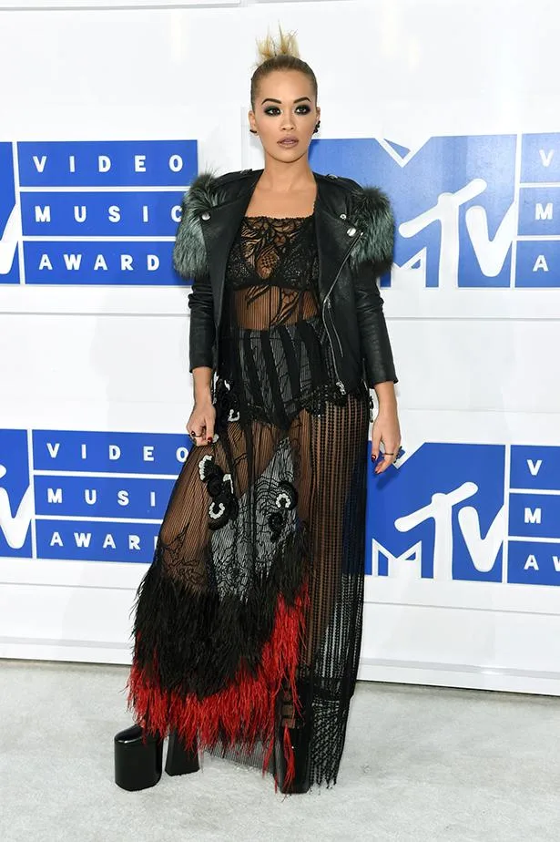 Person in a sheer black dress with red accents and a leather jacket at the MTV Video Music Awards.