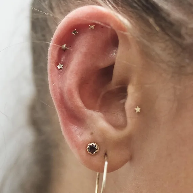 Close-up of an ear with multiple star-shaped piercings and a small hoop earring.