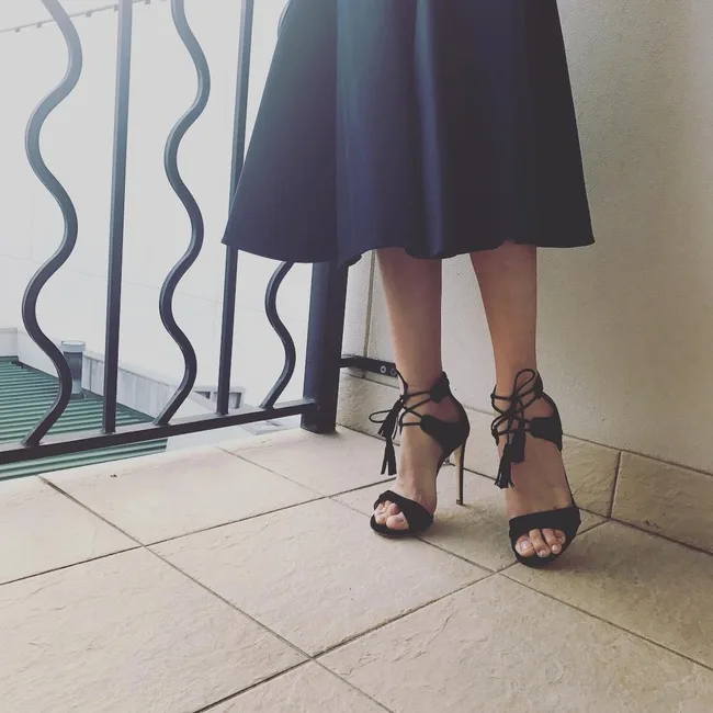 Woman in black dress and lace-up high heels standing on a tiled balcony.