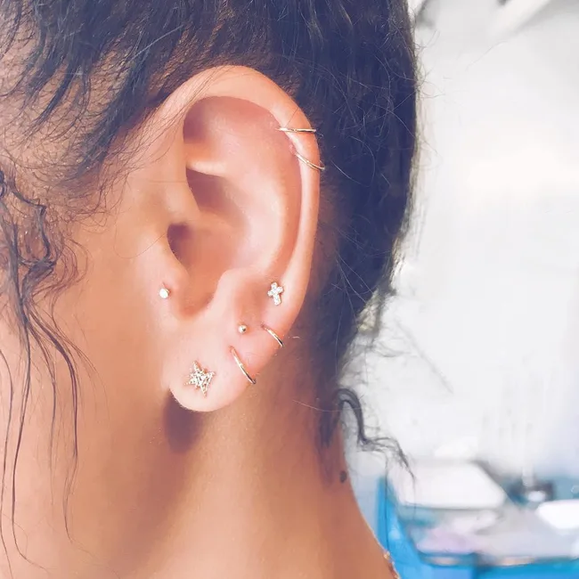 Close-up of a woman's ear with multiple piercings, featuring various small earrings and hoops.