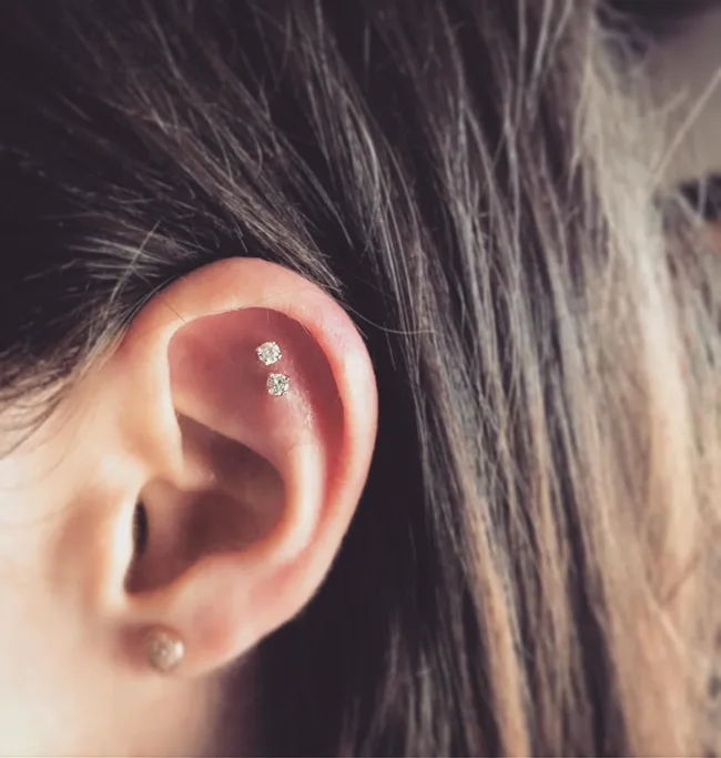 Close-up of an ear with two helix piercings featuring small diamond studs.