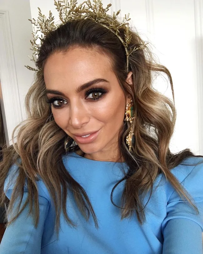 A woman with wavy hair wearing a gold crown and blue top, smiling.