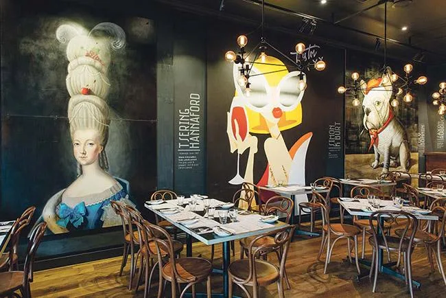 Dining area with mural featuring a woman in period costume, modern abstract art, and a dog in uniform on the walls.