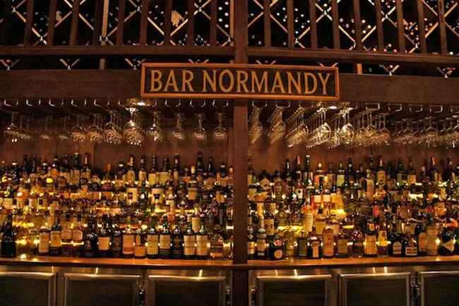 Bar Normandy with shelves of various liquor bottles and hanging wine glasses.