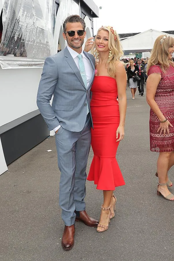 Man in grey suit and sunglasses with woman in red dress posing at an outdoor event.